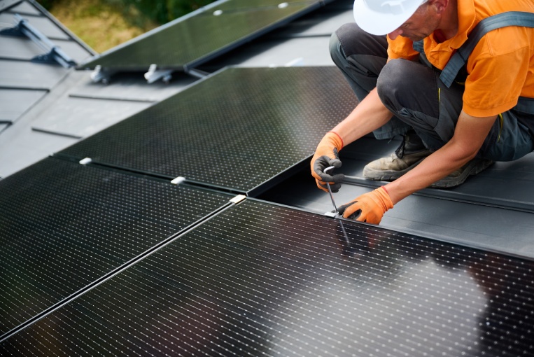 Worker building photovoltaic solar panel system on rooftop of house. Man engineer in gloves installing solar module with help of hex key outdoors. Alternative and renewable energy generation concept.