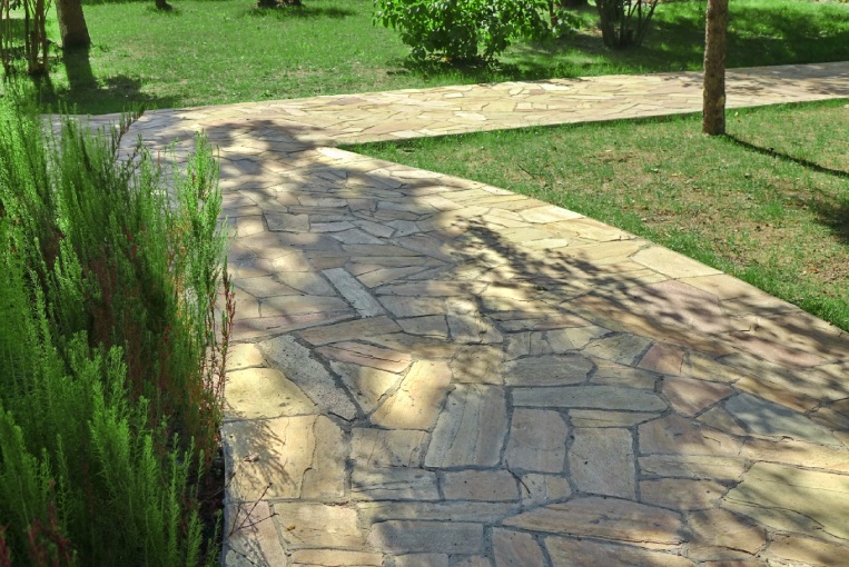 Garden landscaping with Pave from Tiled Limestone. Backyard Garden Shaded Footpath from Tiled Stone Slabs. Flagstone Walkway in The Garden. Shady Pathway From Stone Tiles In The Park.