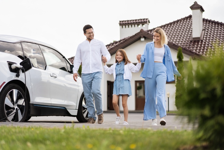 Happy Family Walking Together Near Electric Car Outside Modern Home