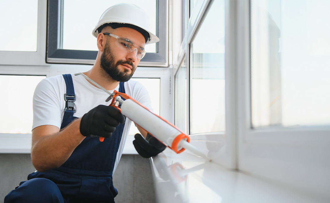 A worker in overalls and a hard hat applies spray paint, highlighting the hidden costs of cheap windows in custom homes.
