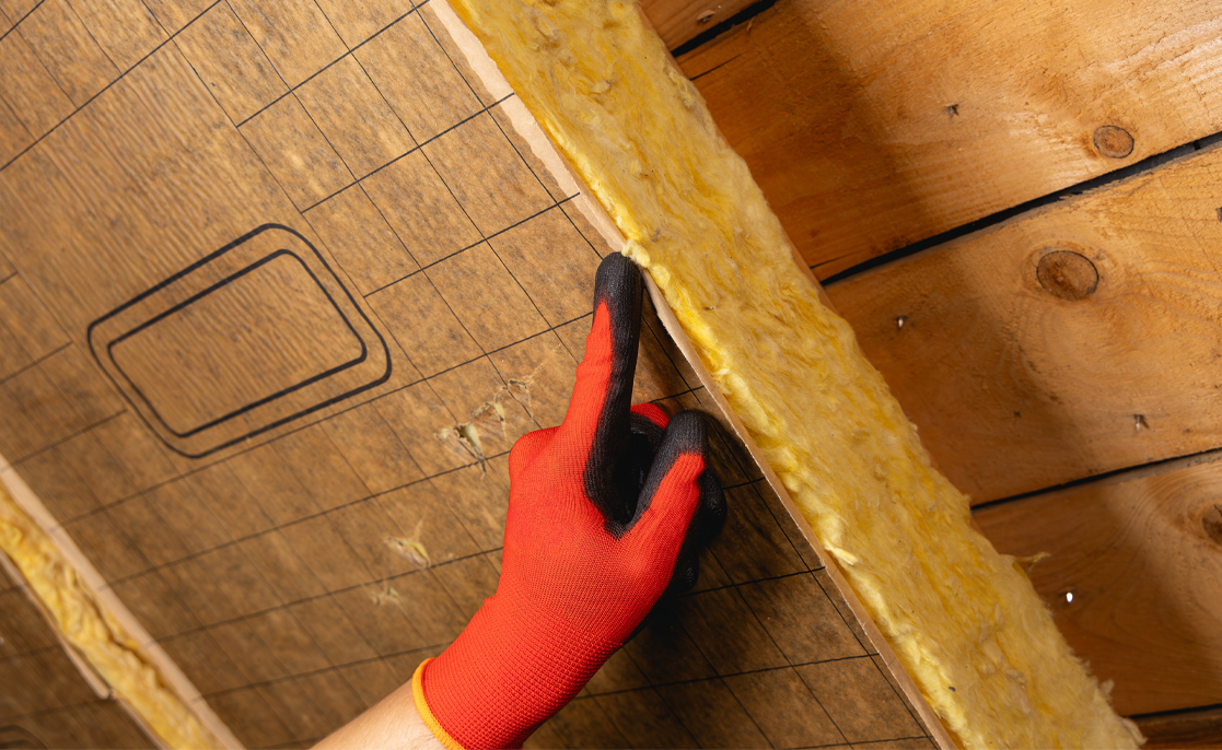 A technician installing fiberglass insulation in the attic to limit heat loss.