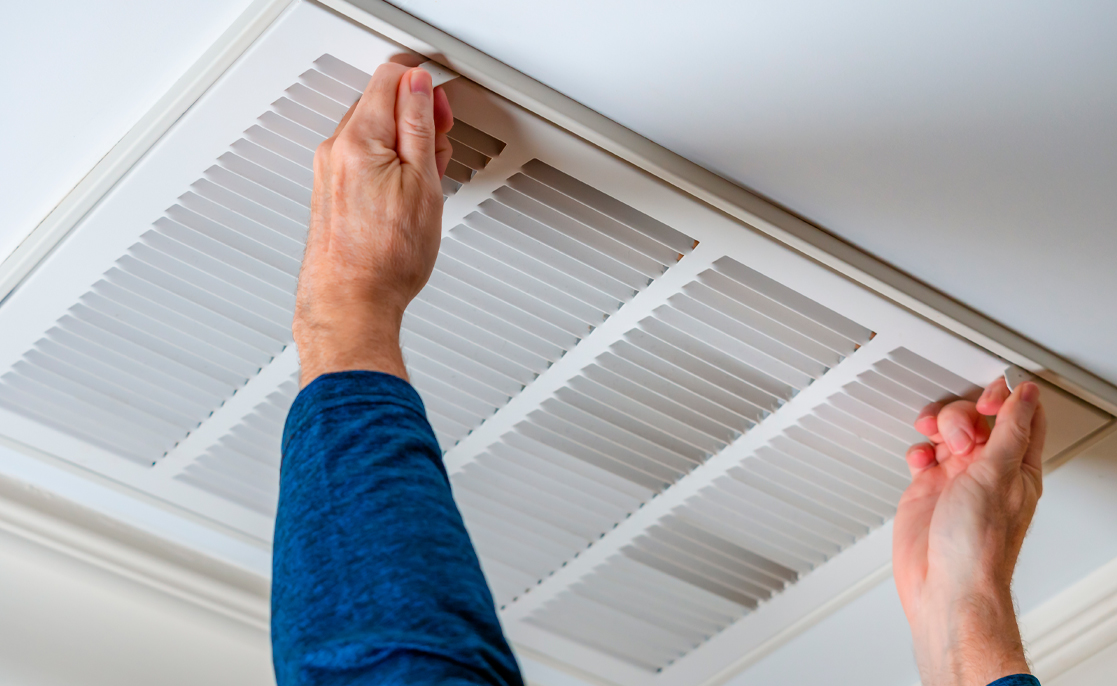 Man opening ceiling air vent to replace dirty HVAC air filter. Home air duct system maintenance for clean air.