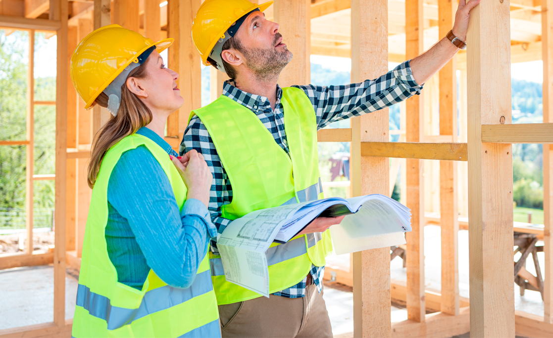 Construction engineer and architect consult plans on building site of wood framing house under construction